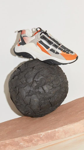 Studio shot of a fashion sneaker balanced on a dark stone sphere and a pink stand against a white backdrop.