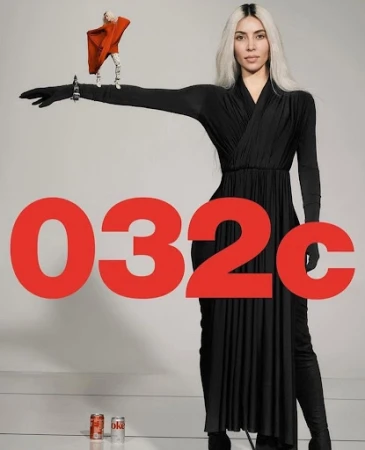 Adult woman in long black dress poses indoors with a small doll wearing an orange cape and two cans of Coca-Cola in the background.