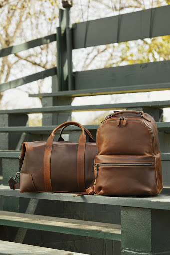 Brown leather duffel bag and backpack sit on green stadium steps in outdoor setting, conveying style and functionality.