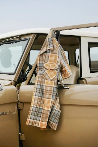 Tan SUV's open door showcases a plaid shirt hanging from the window, evoking a casual and vintage aesthetic against an overcast sky.