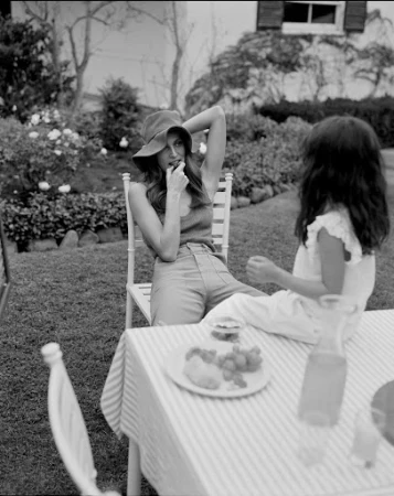 Black and white image of a woman wearing a bucket hat sitting at a garden table with a child