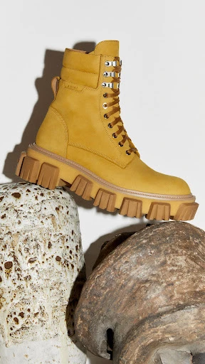 High-fashion yellow lace-up boot with lug sole on decorative stone platforms against a neutral backdrop for footwear advertising.