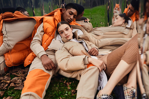 Two fashion models in outdoor fashion shoot, wearing puffer jackets and casual wear, surrounded by multiple reflections of themselves and the environment.