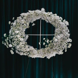 Large white floral wreath arranged on a minimalist metal easel against dark teal velvet curtain background