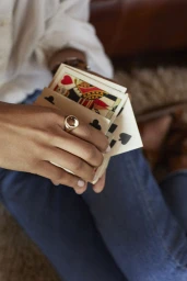 Close-up of a person holding a fan of playing cards, wearing a large gold ring with a clear stone and blue denim jeans.