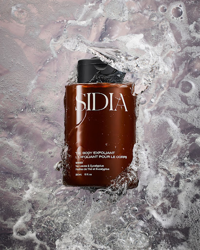 Sidia body exfoliant bottle is centered, surrounded by splashing water creating a refreshing and invigorating visual, studio shot.