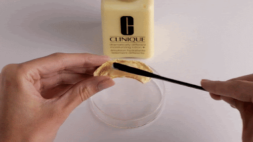Clinique moisturizer application with a spatula on a cotton pad. Features a skincare product, beauty routine and personal care items.