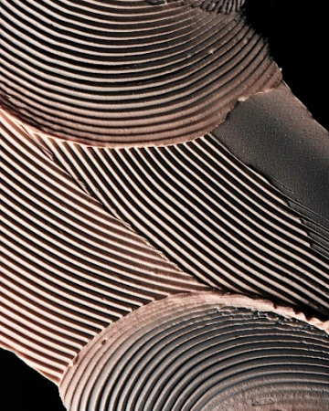 Macro shot of a light brown cosmetic product with lines and ridges against a solid black background, emphasizing texture and detail.
