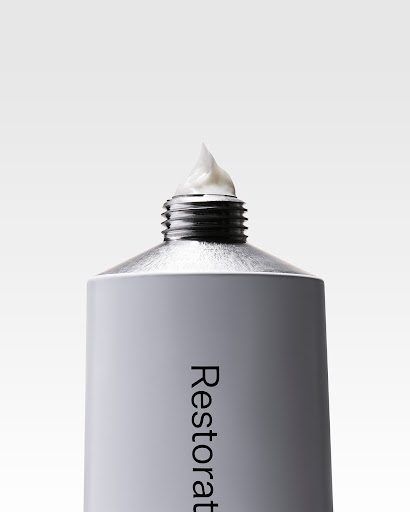 Close-up of a gray and silver metal tube with white cream on top against a white background. Beauty and healthcare product.