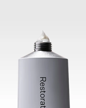 Close-up of a gray and silver metal tube with white cream on top against a white background. Beauty and healthcare product.