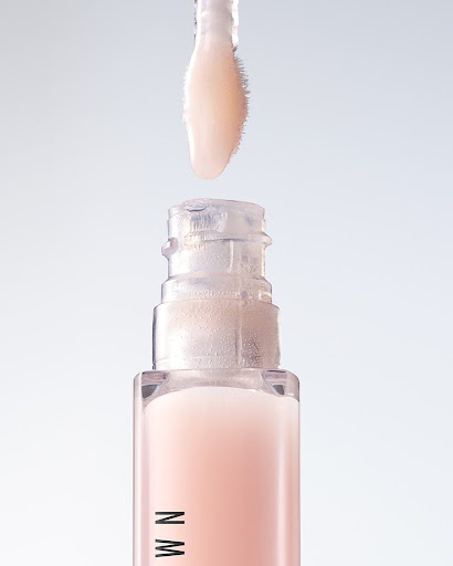 Close-up of lip gloss tube with wand applicator. The lip gloss is a light pink color, and the tube has a clear top and pink base.