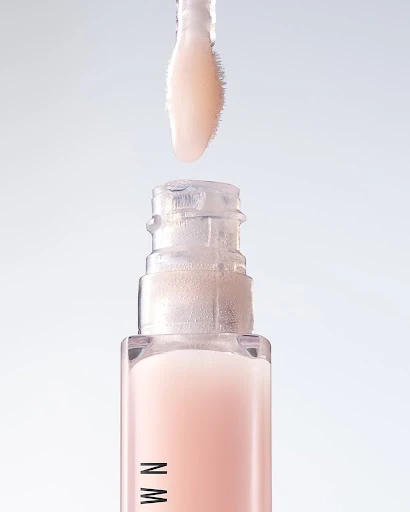 Close-up of lip gloss tube with wand applicator. The lip gloss is a light pink color, and the tube has a clear top and pink base.