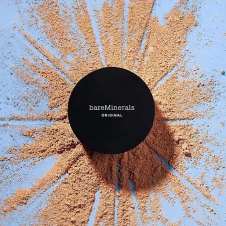BareMinerals Original loose powder foundation with lid, tan powder surrounding the container on a light blue surface.