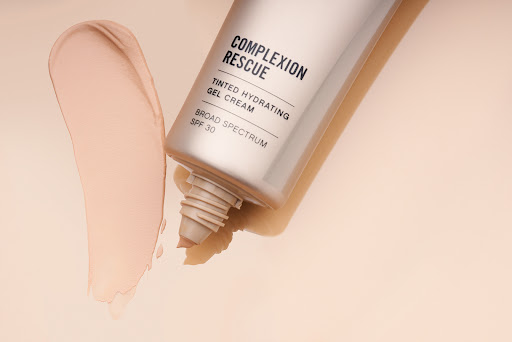 Cosmetics tube and smear of tinted gel cream on a beige backdrop, product shot for beauty or skincare advertising, copy space.