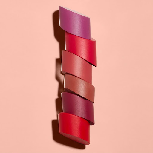 Tower of assorted lipstick samples in red, pink, and purple tones. Beauty advertising with product display on pink backdrop.
