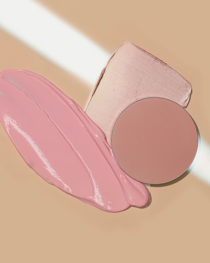 Close-up of pink and neutral-toned beauty products with creamy textures and minimalist presentation against a tan backdrop.