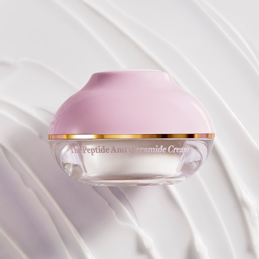 Close-up shot of a container of white cream with a pink lid against a white background with cream-like swirls for visual texture.