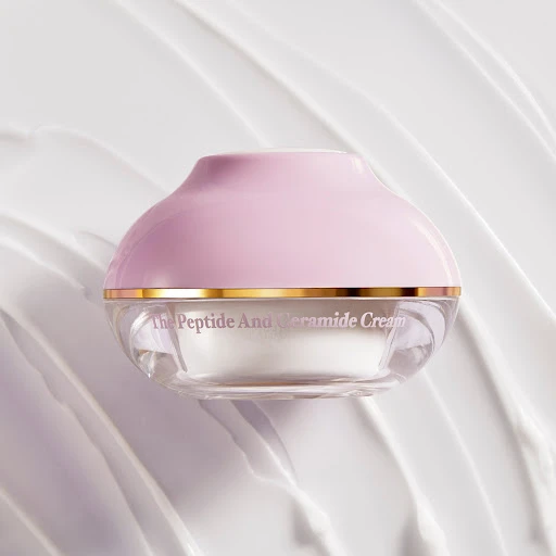 Close-up shot of a container of white cream with a pink lid against a white background with cream-like swirls for visual texture.