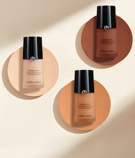 Three bottles of Luminous Silk foundation by Giorgio Armani on round pedestals in a beauty product shot with a neutral background.