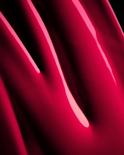 Macro shot of smooth glossy hot pink liquid cosmetic texture with sharp specular highlights
