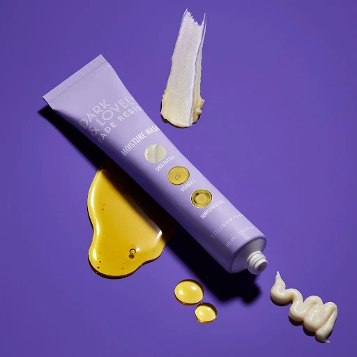 Dark & Lovely Fade Resist moisture mask in a purple tube on a purple background with drops of serum and smears of product.