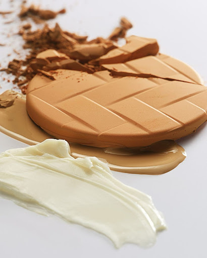 Tan and white smears of cosmetics including face powder and cream foundation with a leaf pattern on a white background.