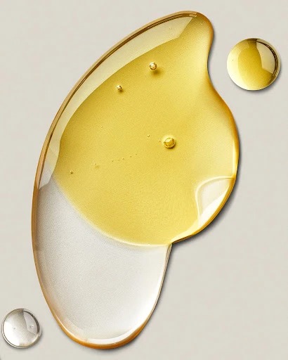 Close-up studio shot of transparent liquid with gold and silver tints in abstract curved shapes on a neutral background, drops included.