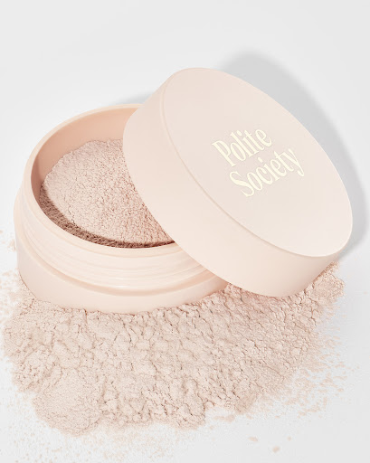 Close-up of a jar of setting powder by Polite Society with lid ajar, on a white background. Beauty product for makeup.