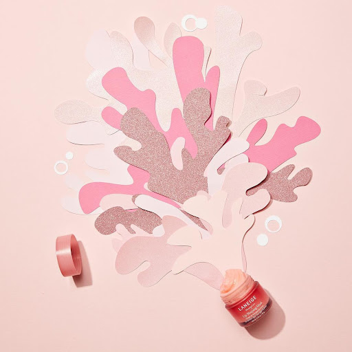 Pink lip sleeping mask jar with paper cutouts in studio. Laneige brand skincare product for beauty, health, and well-being.