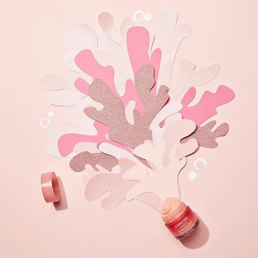 Pink lip sleeping mask jar with paper cutouts in studio. Laneige brand skincare product for beauty, health, and well-being.