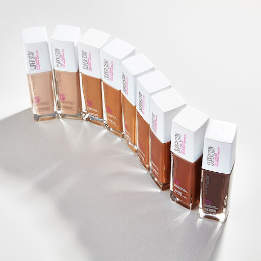 Collection of Maybelline Super Stay foundation bottles in various shades arranged on a white surface with soft lighting, showcasing product range.