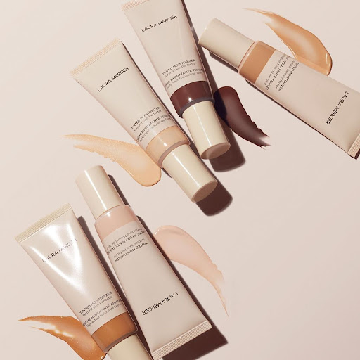 Arrangement of Laura Mercier tinted moisturizers in various shades, displayed on a light surface, showcasing diverse skin tone options.