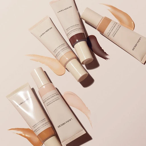 Arrangement of Laura Mercier tinted moisturizers in various shades, displayed on a light surface, showcasing diverse skin tone options.