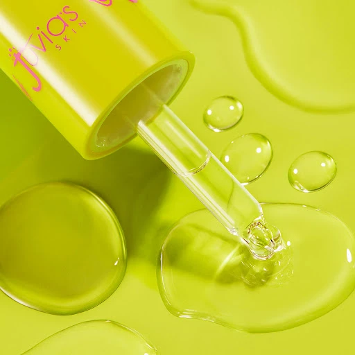 Close-up of a Juvia's Skin serum bottle and dropper with clear serum drops on a light green surface for beauty product promotion.