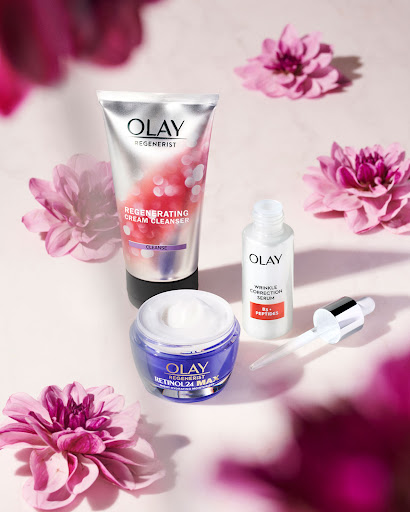 Olay skincare product line including Regenerist Cream Cleanser, Retinol 24 MAX face moisturizer, and Wrinkle Correction Serum on pink backdrop.