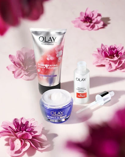 Olay skincare product line including Regenerist Cream Cleanser, Retinol 24 MAX face moisturizer, and Wrinkle Correction Serum on pink backdrop.