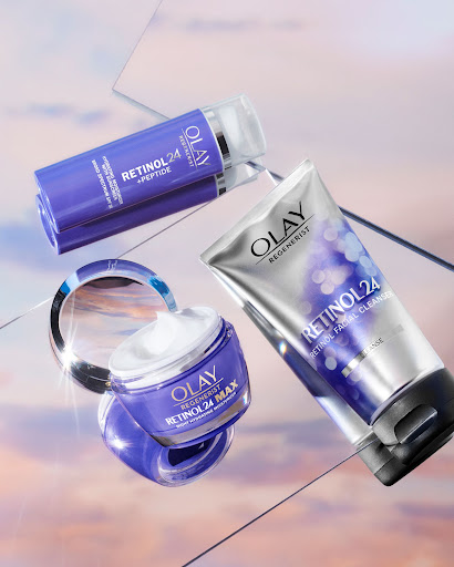 Olay Retinol 24 MAX moisturizer, Retinol 24 + Peptide serum, and Retinol Facial Cleanser arranged on a reflective surface.