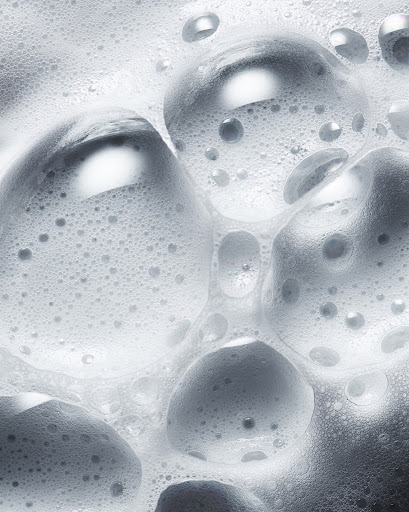 Close-up shot of white soap suds and bubbles creating a dense foam pattern, suitable for beauty, hygiene, or cleaning product imagery.