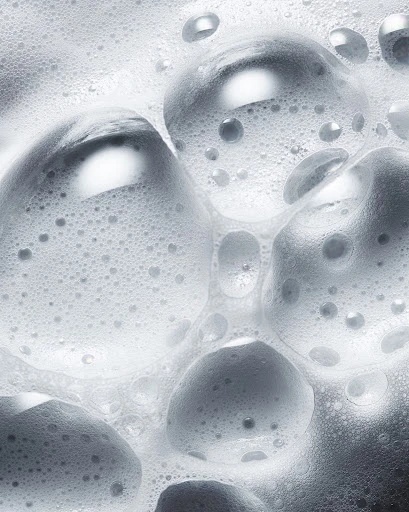 Close-up shot of white soap suds and bubbles creating a dense foam pattern, suitable for beauty, hygiene, or cleaning product imagery.
