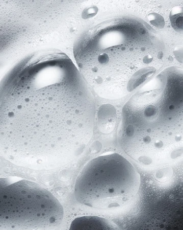 Close-up shot of white soap suds and bubbles creating a dense foam pattern, suitable for beauty, hygiene, or cleaning product imagery.