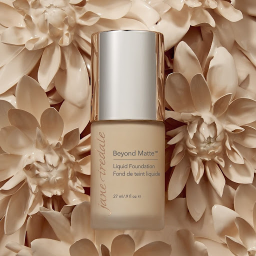 Close-up of a bottle of Jane Iredale Beyond Matte liquid foundation set against a background of decorative floral elements.