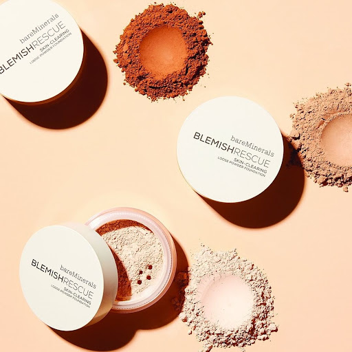 BareMinerals Blemish Rescue skin-clearing loose powder foundation in various shades, arranged on a peach-colored surface in a studio setting.