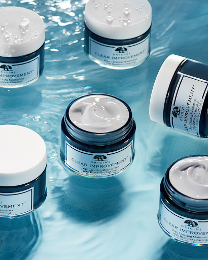 Several jars of Origins Clear Improvement moisturizer with bamboo charcoal are displayed in a light blue setting with water droplets.
