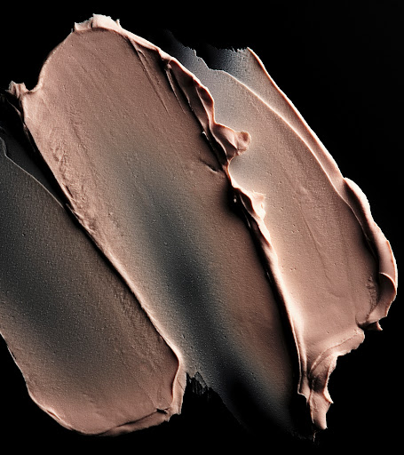 Close-up of textured beige cosmetic product on black. Swirls of a creamy material create an abstract, visually appealing design.