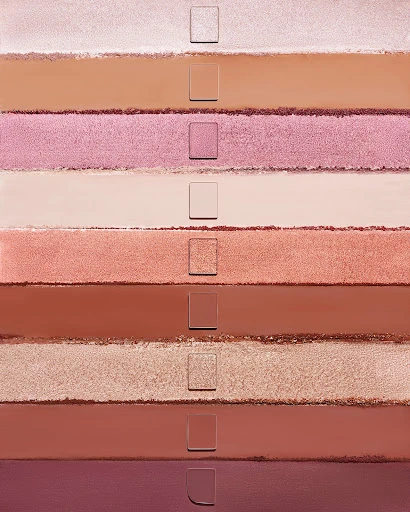 Close-up of ten parallel swatches of various cosmetic powder shades from light peach and pink to darker brown and plum hues.