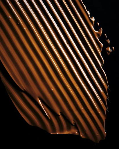 Brown liquid makeup or cream foundation swatch with linear texture against black background in a vertical format for beauty concepts.