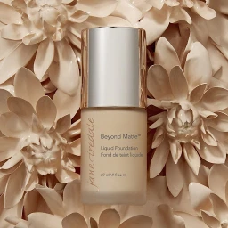 A cylindrical foundation bottle with silver cap positioned vertically among sculpted beige floral petals in New York