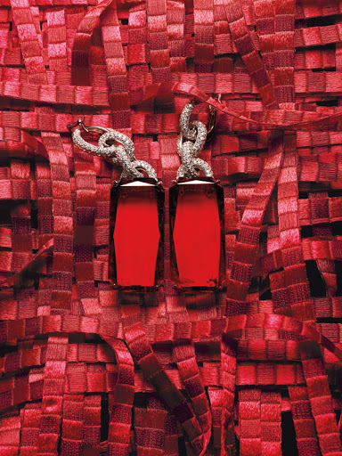 A pair of luxury earrings featuring red gemstone pendants, intricate silver filigree, and a red woven background in a studio setting.