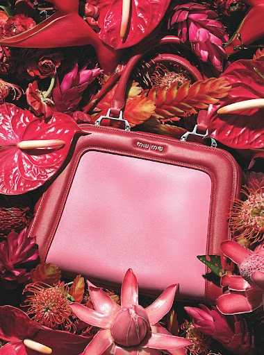 Elegant pink Miu Miu handbag surrounded by vibrant red Anthurium flowers and other tropical foliage in a high-fashion still life.