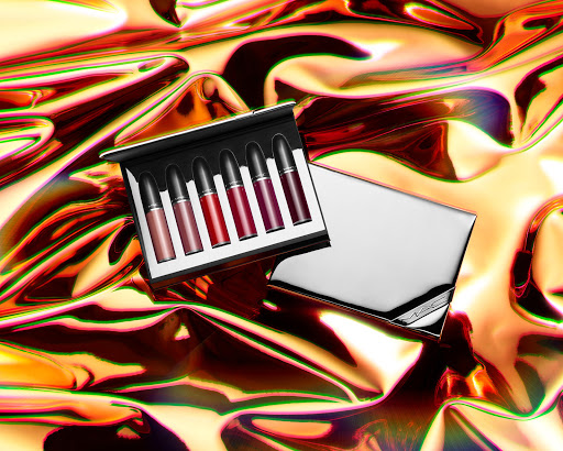 MAC lipstick collection in a black case with a reflective silver lid on a shiny orange metallic fabric background.